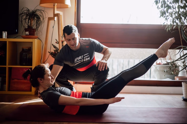 Kévin Richard accompagne une cliente allongée sur un tapis, jambes tendues, pour une séance de Pilates à domicile