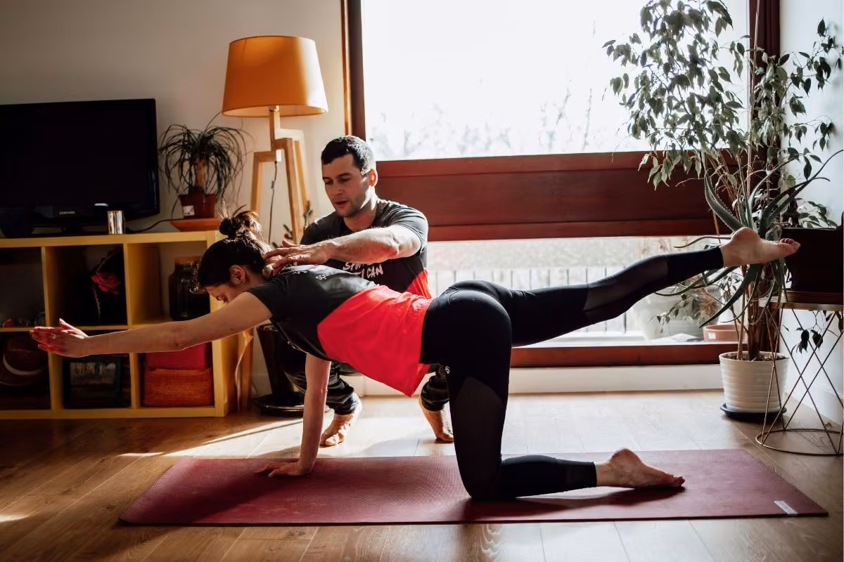 Cliente en gainage à quatre pattes, bras et jambe opposés tendus, coach attentif