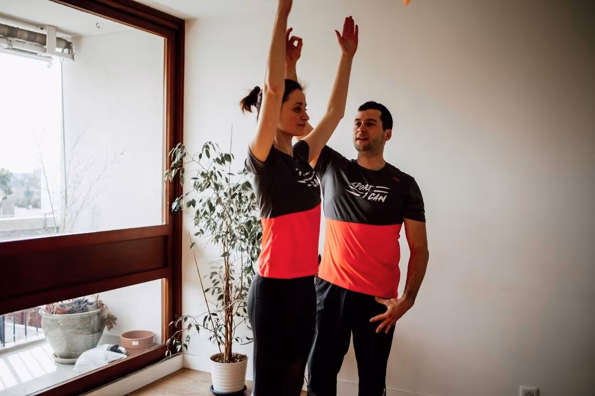 Coach et cliente bras levés, souriants, pendant une séance à domicile