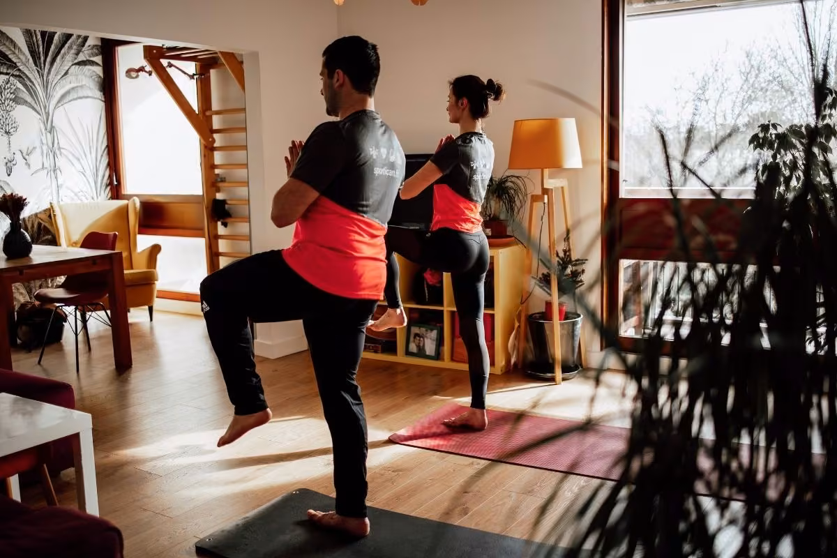 Exercice d'équilibre genou levé, coach et cliente côte à côte dans un salon