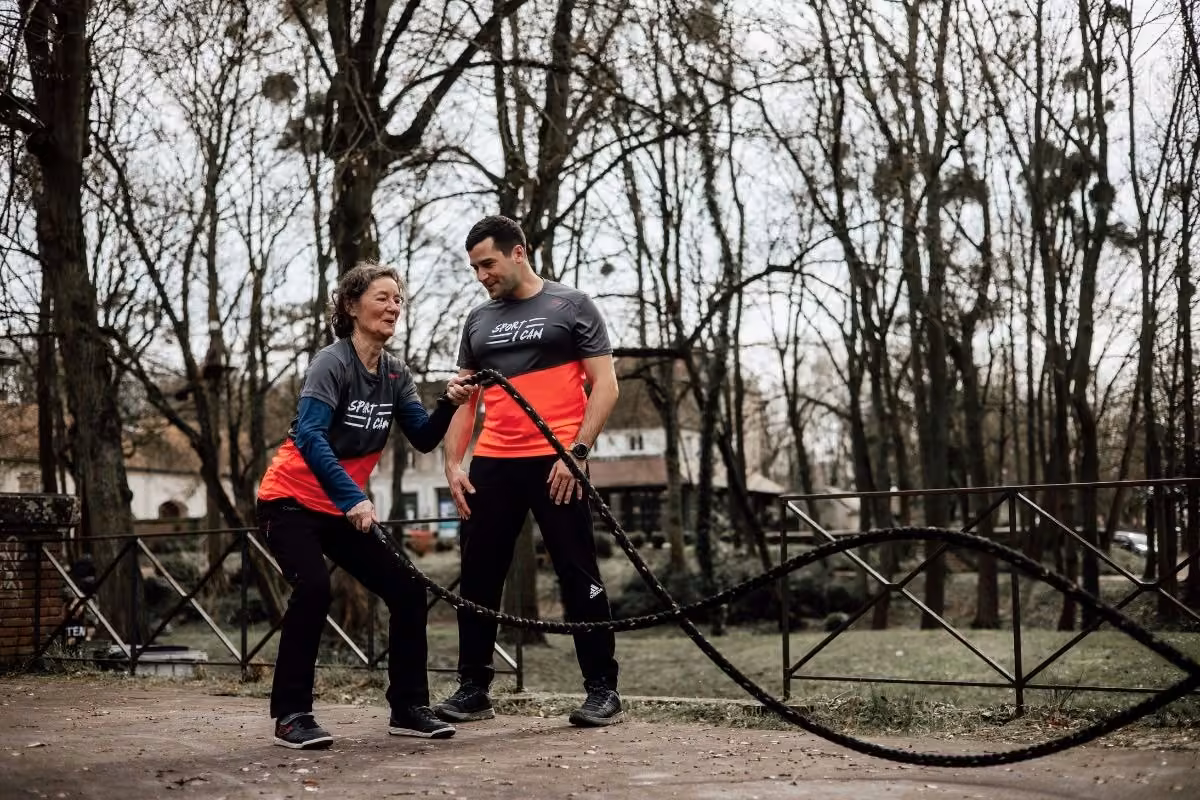Participante souriante à la corde ondulatoire avec son coach dans un parc
