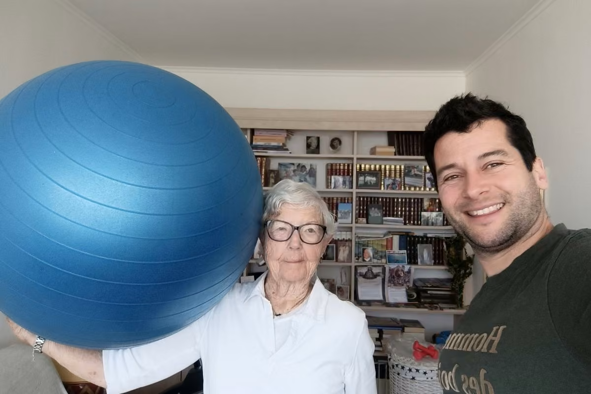 Séance à domicile avec une cliente senior tenant un ballon de gym, coach souriant