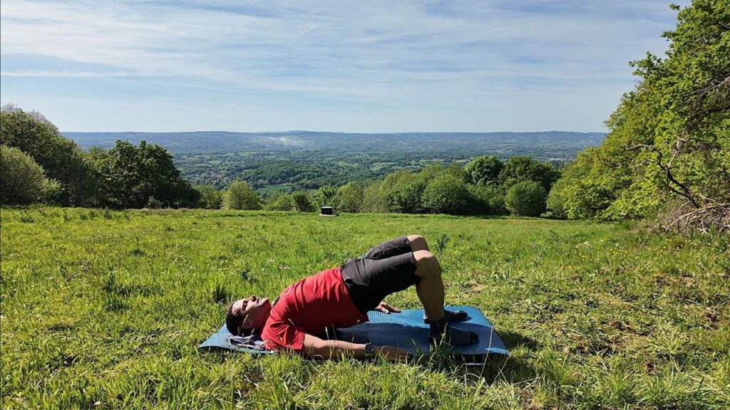 Le coach allongé sur le dos monte le bassin en pont, dans une prairie face à la vallée