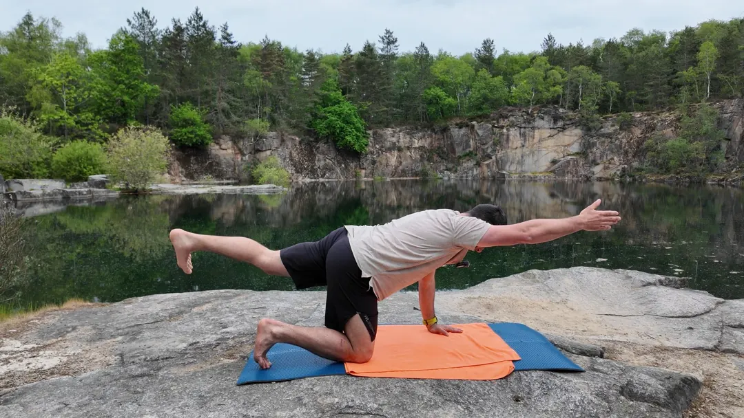 À quatre pattes sur un rocher au bord de l’eau, le coach tend le bras droit devant et la jambe gauche derrière