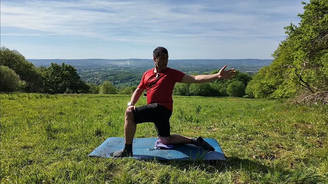 Un genou au sol en fente, le coach ouvre le bras vers l’arrière et tourne le regard pour mobiliser le haut du dos