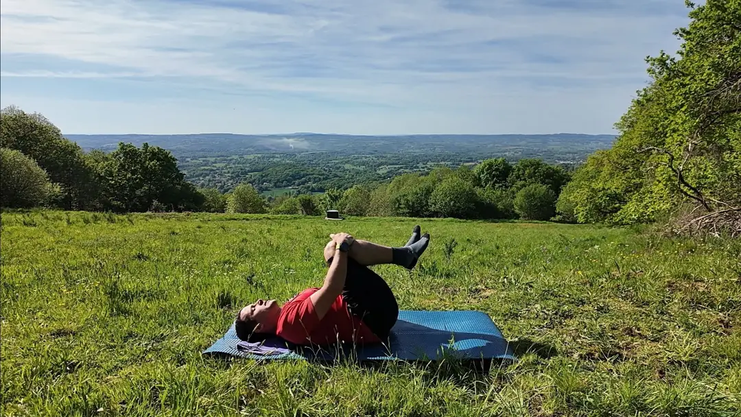 Allongé sur le dos dans l’herbe, le coach ramène les genoux vers la poitrine, mains sur les genoux