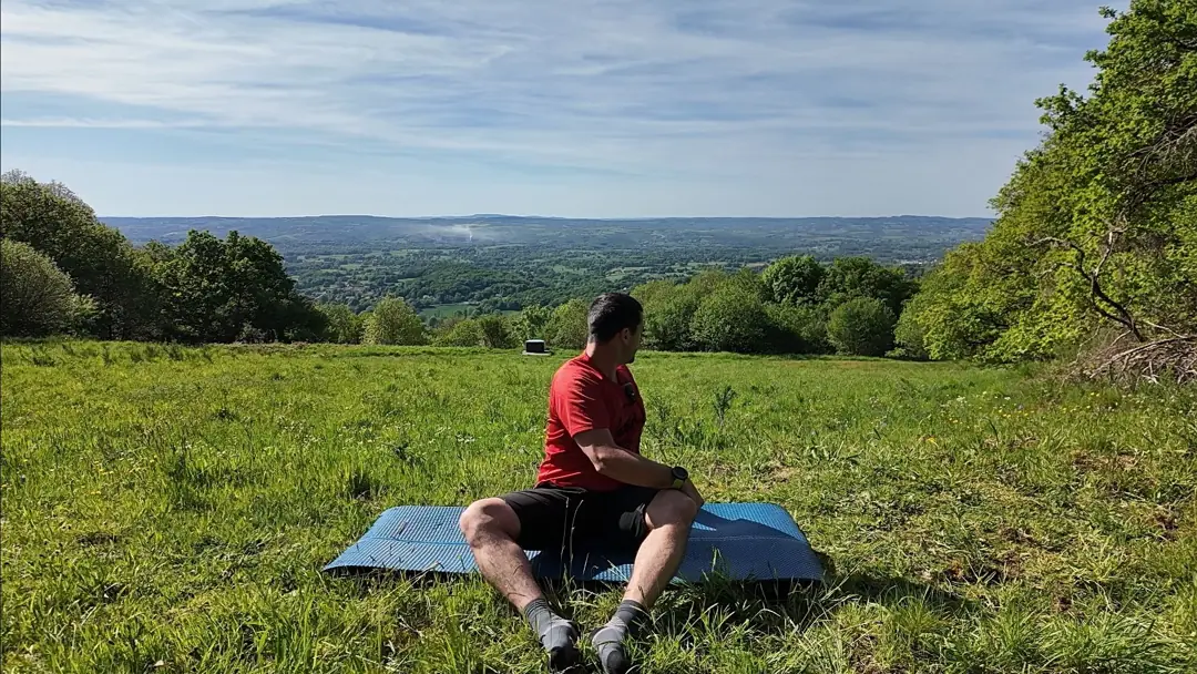Assis sur un tapis, pieds écartés, le coach fait pivoter les genoux d’un côté pour mobiliser les hanches