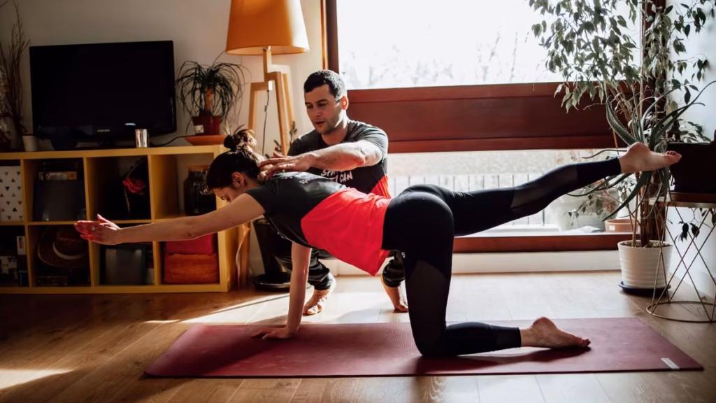 Le coach guide une cliente dans un exercice d’équilibre à quatre pattes, Pilates à domicile