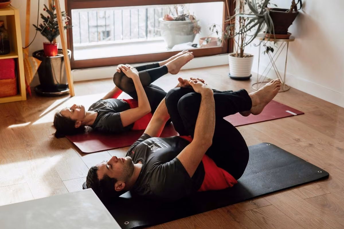 Pilates à domicile : exercice genoux au thorax, coach et cliente sur tapis