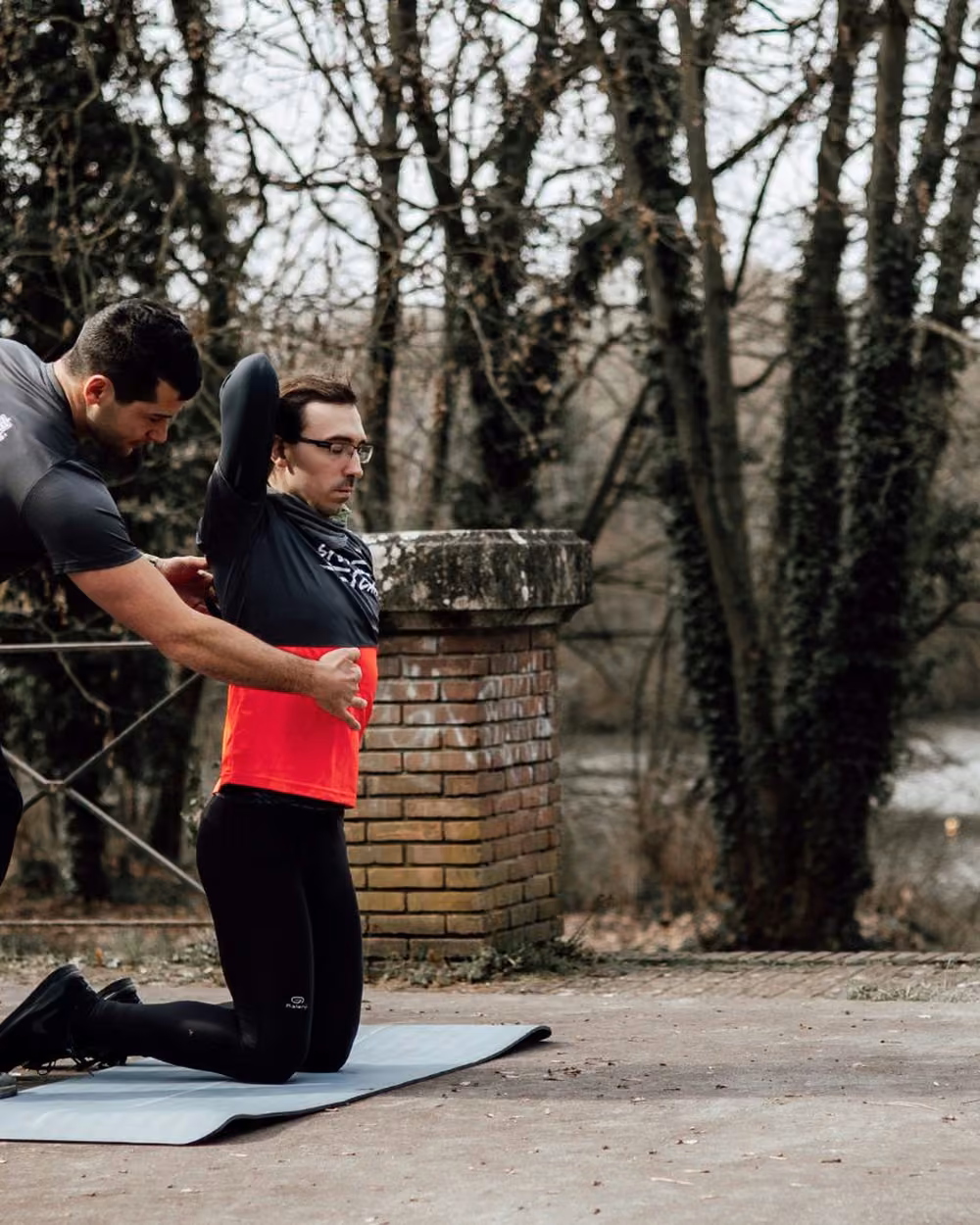 Le coach ajuste la posture d’un client agenouillé lors d’une séance en plein air au bord d’un lac